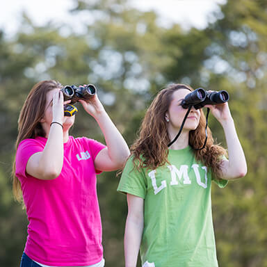 two students outside looking through binoculars